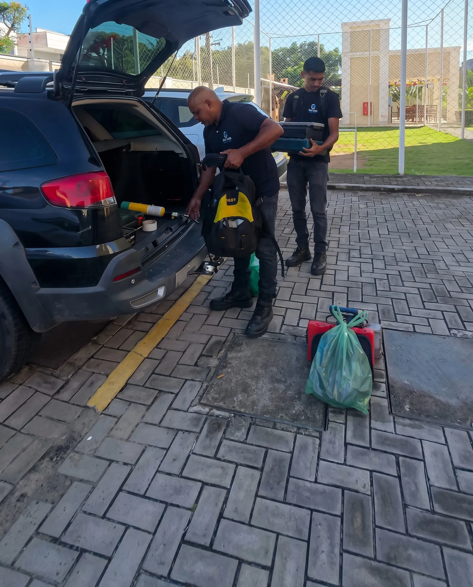 Dois técnicos da Ideal Clima tirando ferramentas do porta-malas do carro da empresa