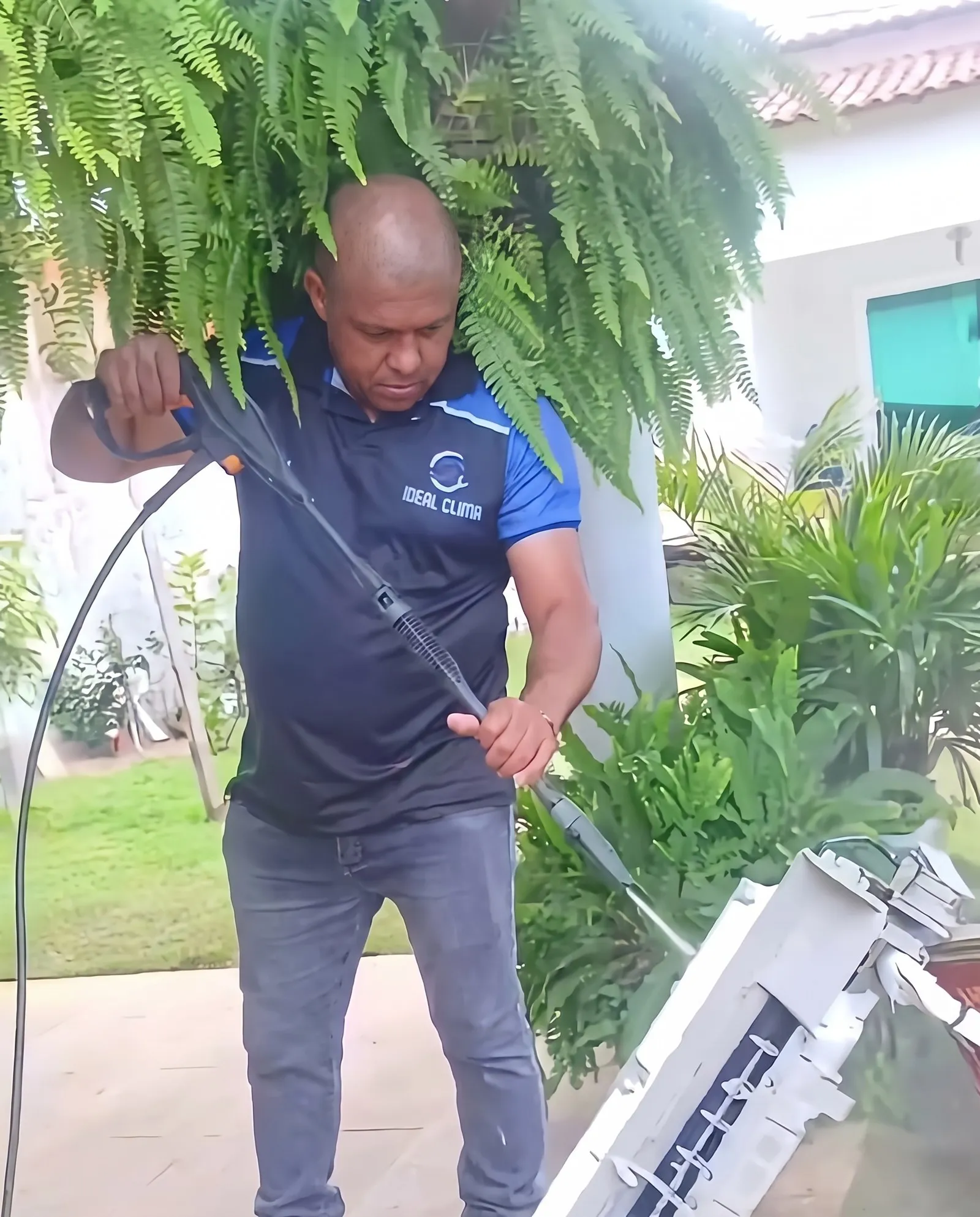 Técnico lavando a unidade interna com jato de alta pressão em um jardim